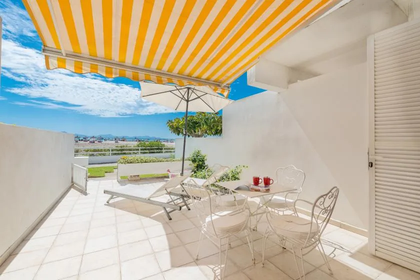 Una terraza soleada con suelo de baldosas y asientos al aire libre bajo un toldo a rayas.