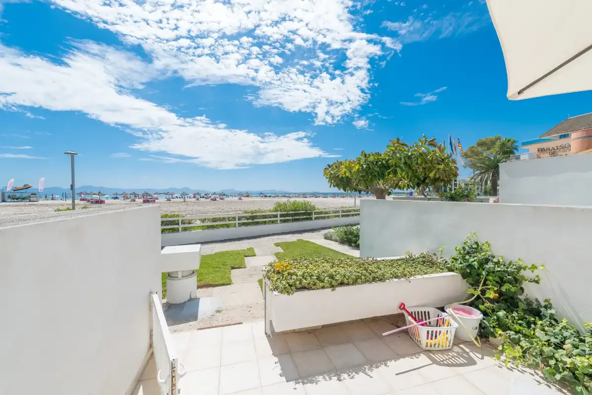 Una terraza soleada al aire libre mira hacia zonas verdes ajardinadas y el paseo marítimo a lo lejos.