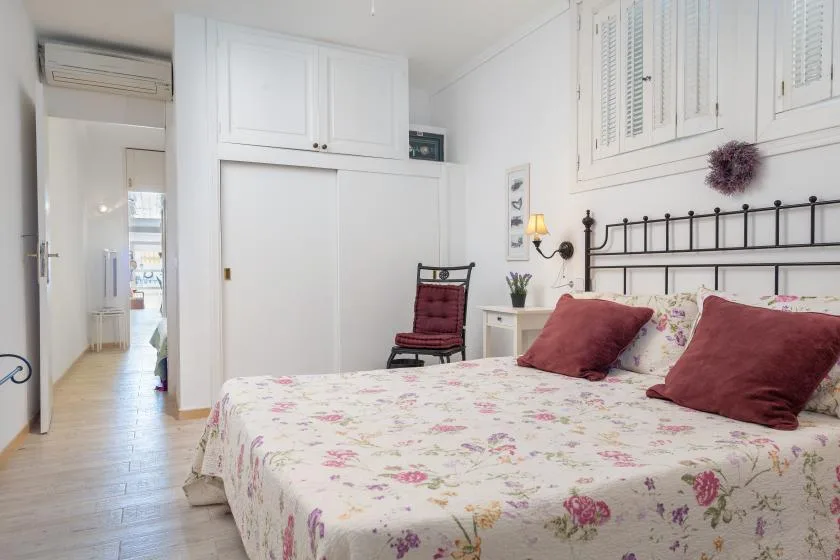 Un dormitorio luminoso con una colcha floral, almohadas rojas y un cabecero de metal negro.