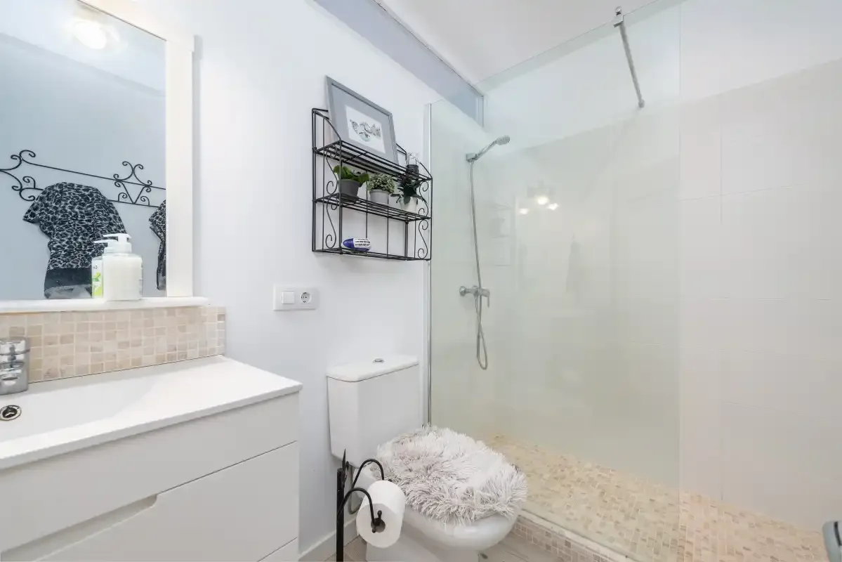 Un baño luminoso con lavabo, inodoro y ducha de cristal.
