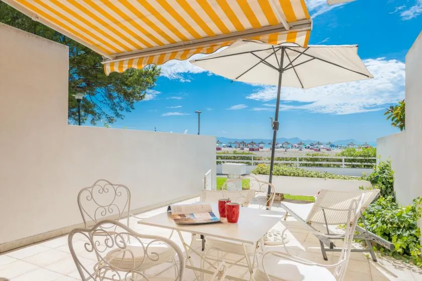 Un patio al aire libre con asientos bajo un toldo a rayas y una sombrilla.