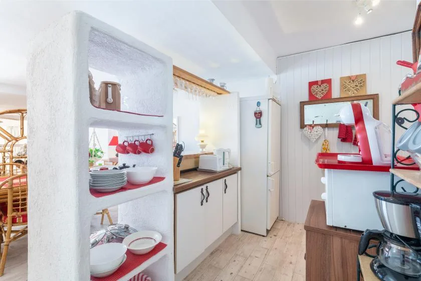 Una cocina compacta con gabinetes blancos, un refrigerador y electrodomésticos rojos sobre la encimera.
