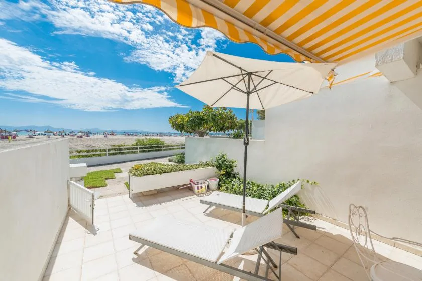 A sunny outdoor terrace with lounge seating, an umbrella, and a striped awning.