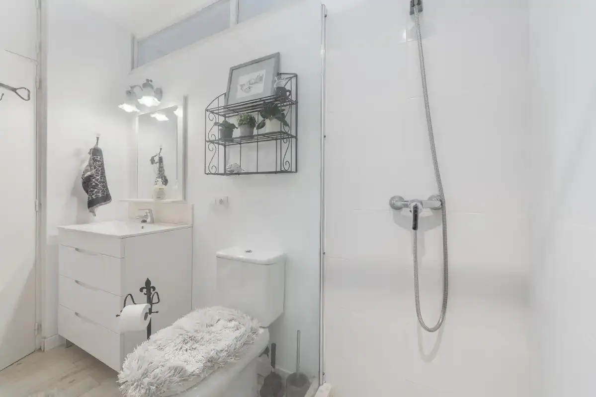 Un baño luminoso con lavabo, inodoro y ducha de pared.