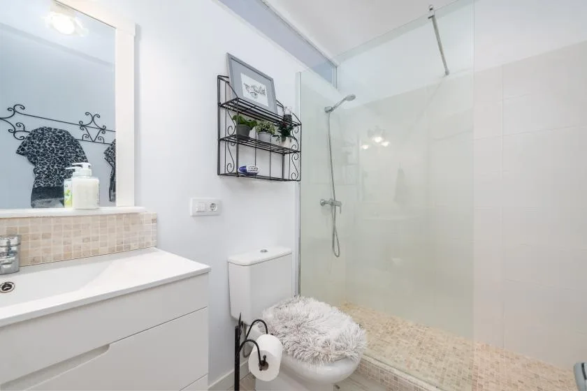 Un baño luminoso con lavabo, inodoro y ducha de vidrio.