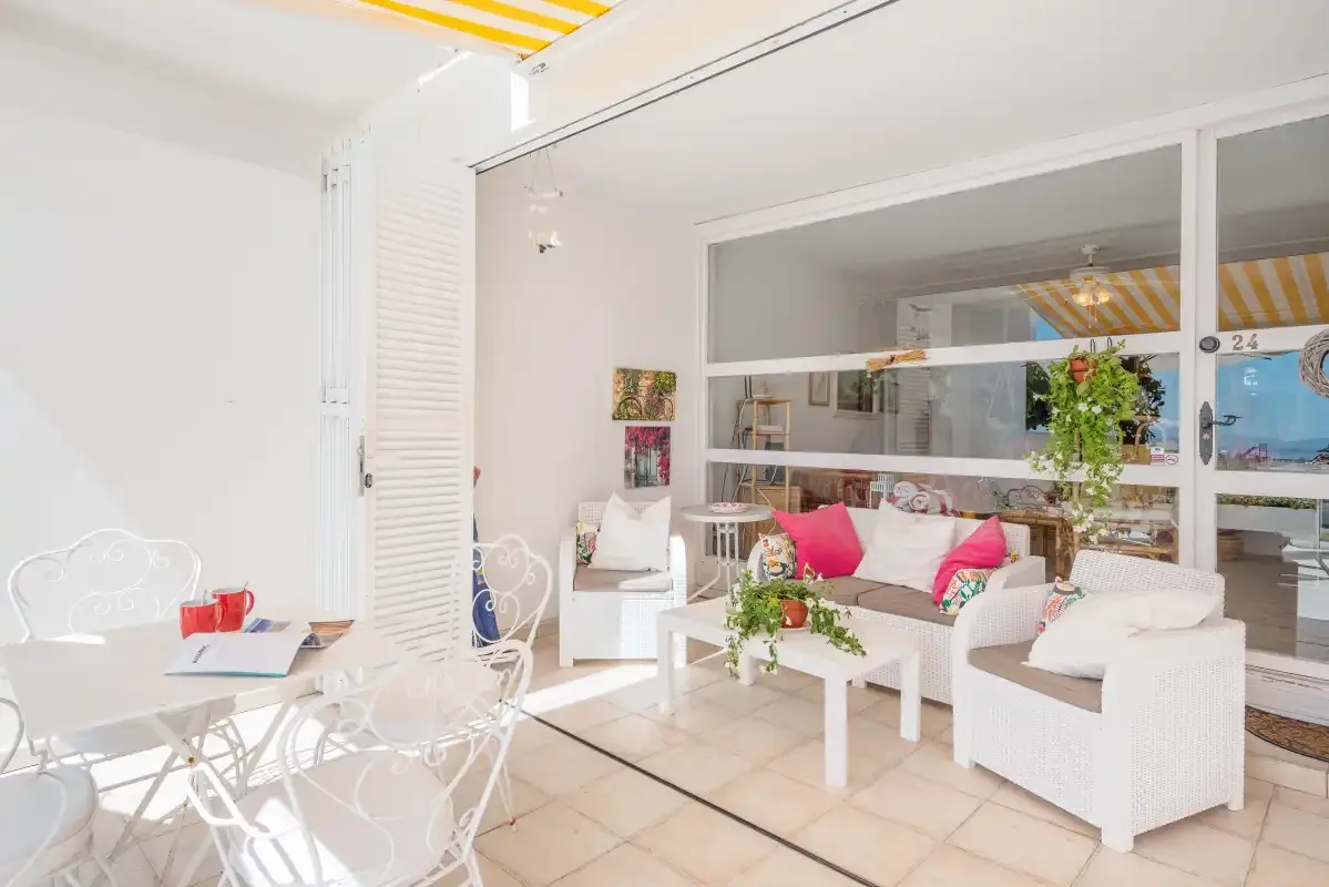 Un luminoso solárium con asientos blancos, una mesa de centro y una zona de comedor.