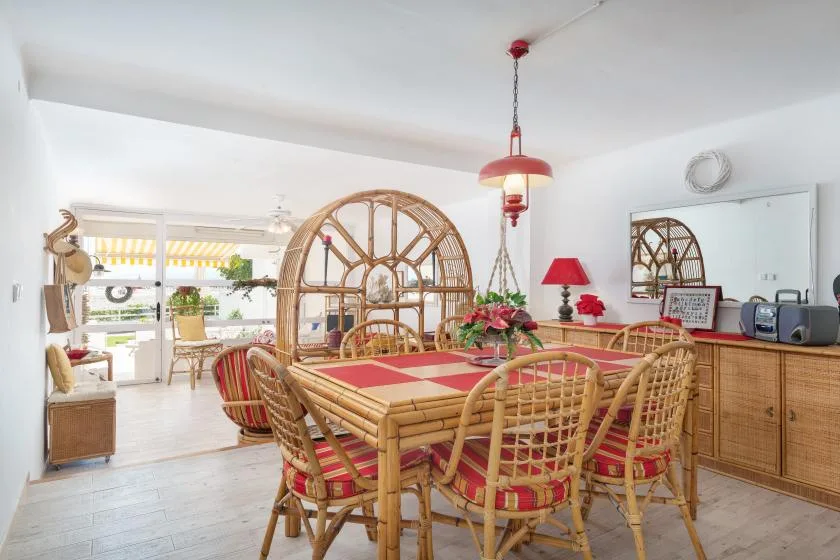 Un comedor luminoso con asientos de mimbre y una gran ventana arqueada.