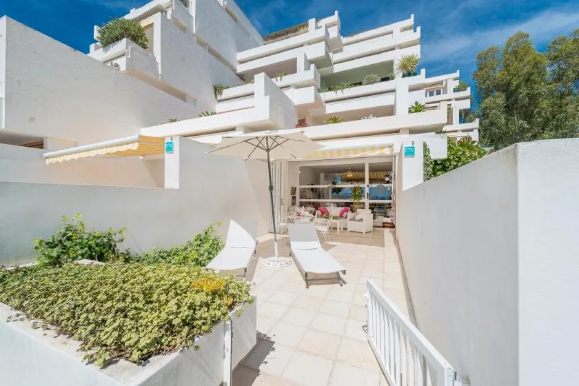 A sunlit patio has lounge seating beneath a large umbrella.