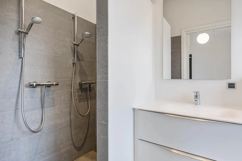 Un baño moderno con una ducha de azulejos y un lavabo blanco.