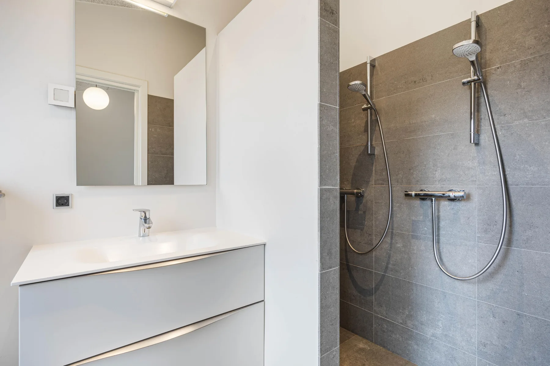 Baño moderno con lavabo y mueble junto a una ducha con azulejos.