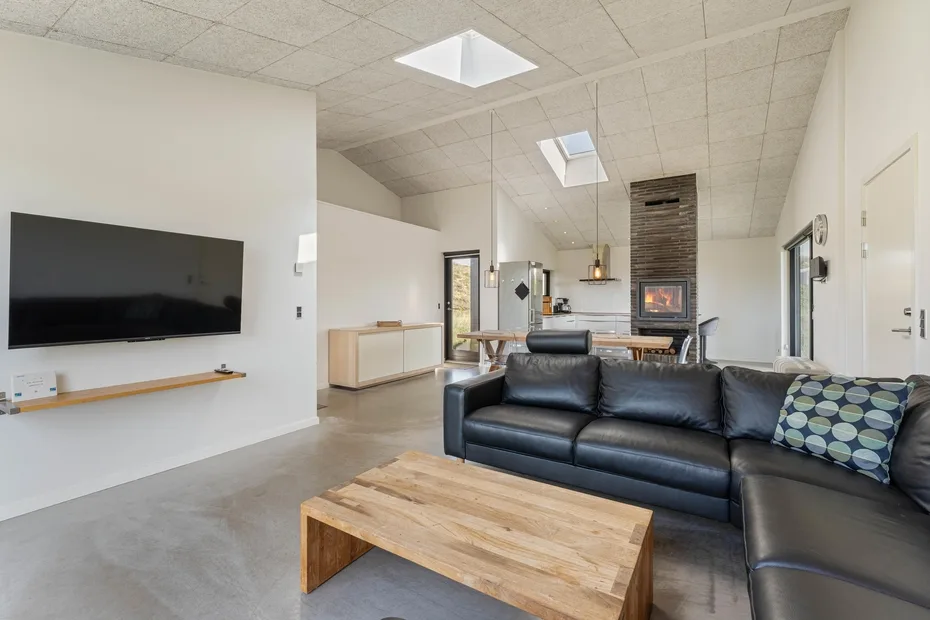 Sala de estar y cocina de concepto abierto con sofá seccional negro y mesa de centro de madera.