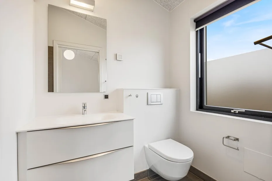 Baño luminoso con lavabo, espejo e inodoro junto a una ventana.