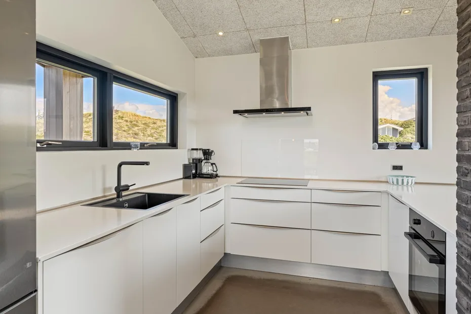 Una cocina moderna y luminosa con gabinetes blancos, fregadero y una placa de cocción central.