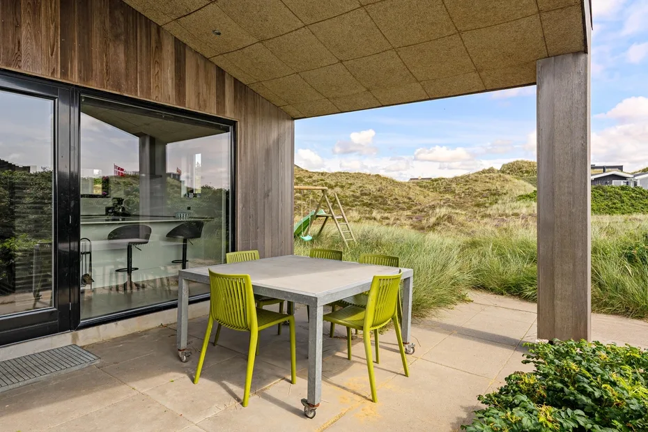 Un patio cubierto con una mesa y asientos de colores vivos da a dunas cubiertas de hierba.