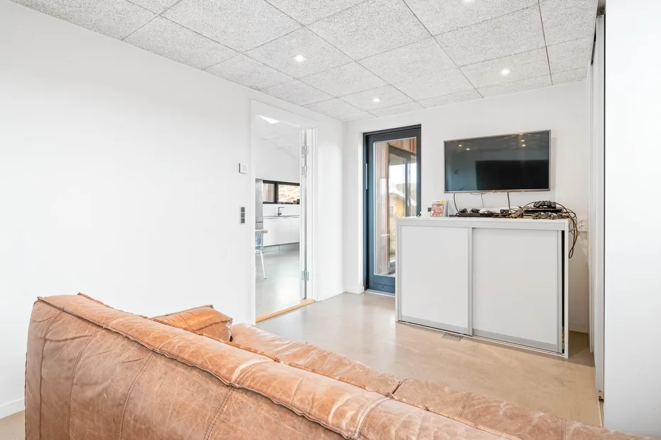 Una sala luminosa con un sofá beige, un televisor y una puerta abierta.
