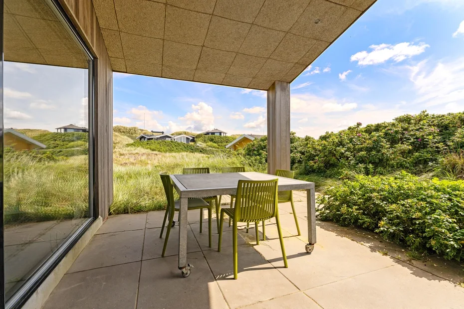 Un patio cubierto tiene una mesa y sillas junto a una pared de vidrio.
