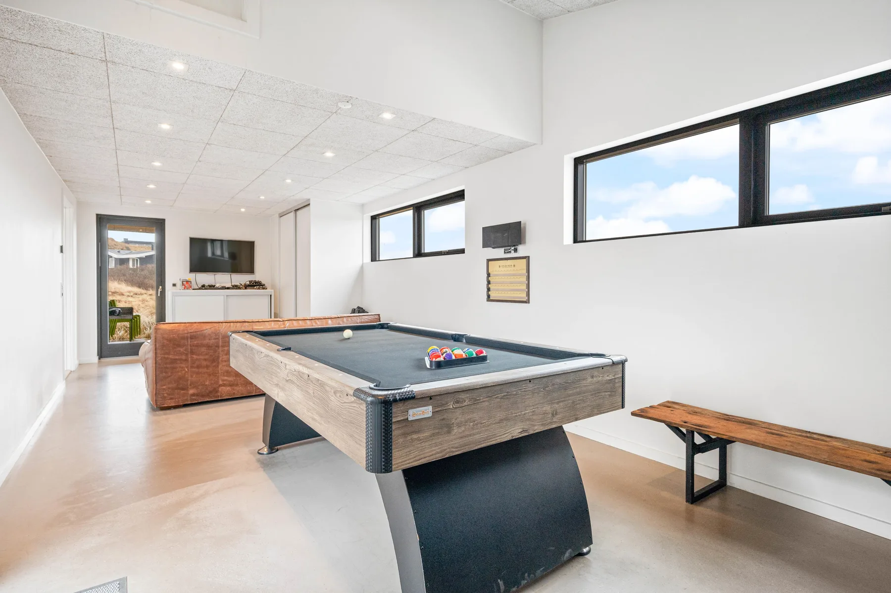Una luminosa sala de recreación tiene una mesa de billar y un banco de madera.