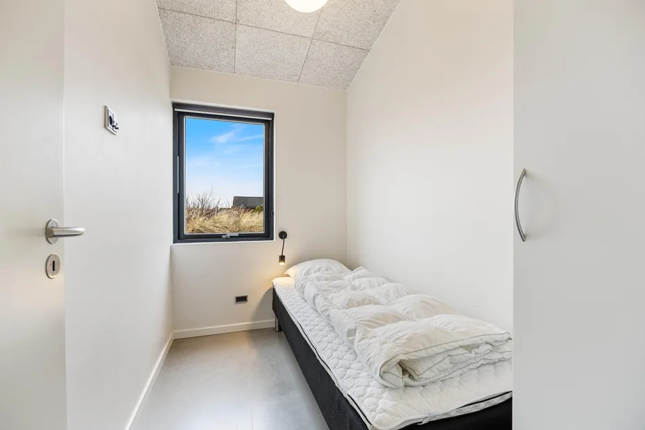 Un dormitorio pequeño con una cama individual bajo una ventana que da a hierba seca.