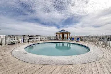 An outdoor pool sits on a wooden deck beneath a cloudy sky.