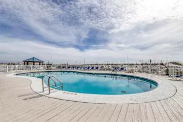 An outdoor swimming pool sits on a broad deck beneath a cloudy sky.