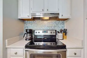Zona de cocina con una estufa bajo gabinetes blancos.