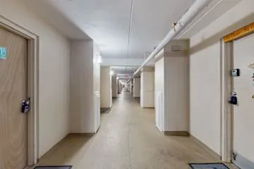 Un largo pasillo interior con puertas y tuberías en el techo.