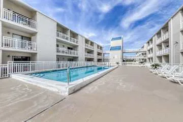 An outdoor swimming pool sits between white multi-story buildings.