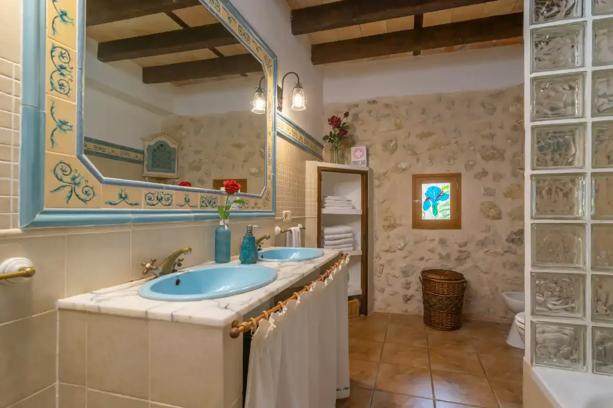 A rustic bathroom with a long vanity, blue sinks, and a glass-block partition.