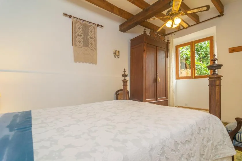A bedroom with a bed, wooden wardrobe, and a window overlooking greenery.