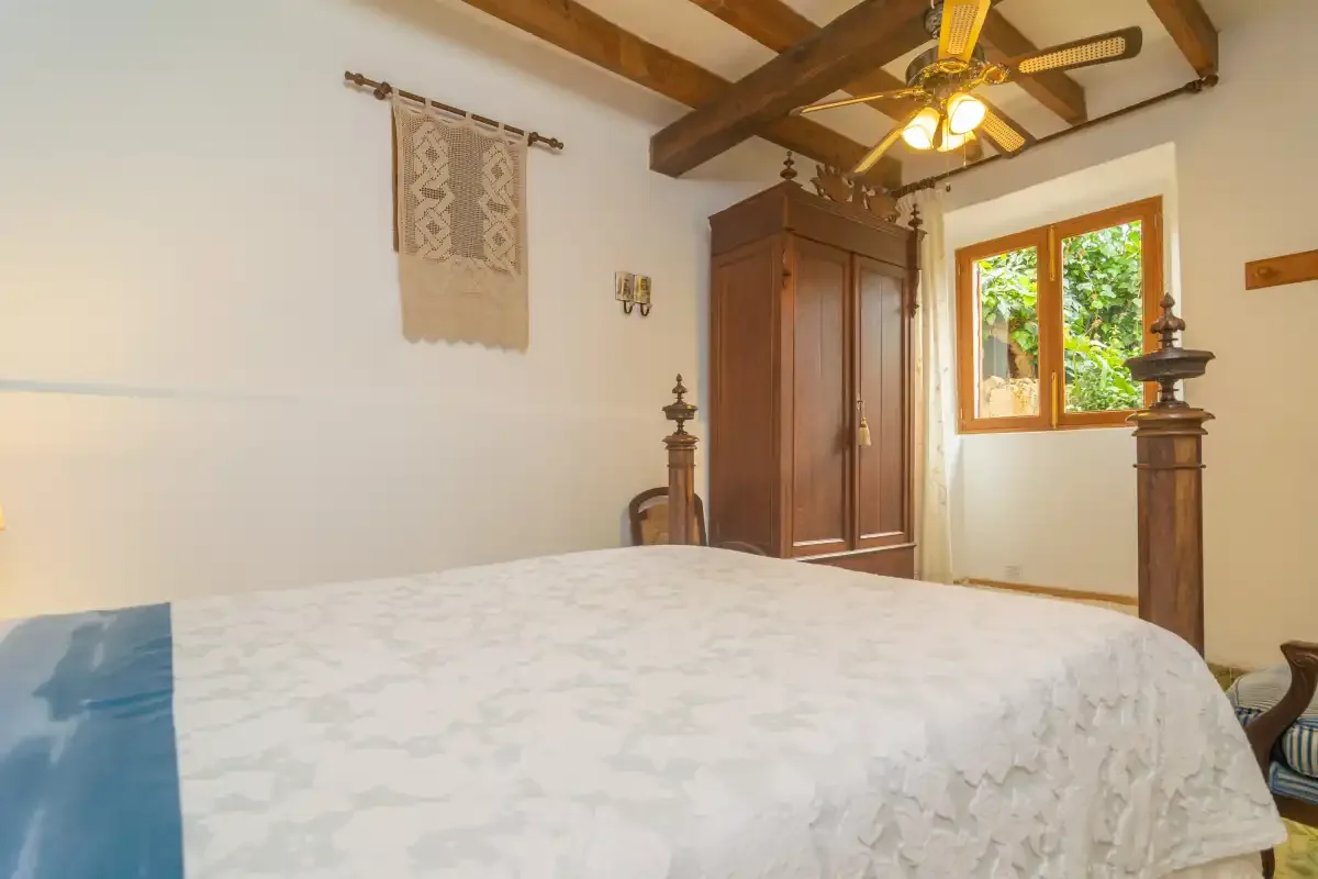 A bedroom with a large bed, wooden wardrobe, and window overlooking greenery.