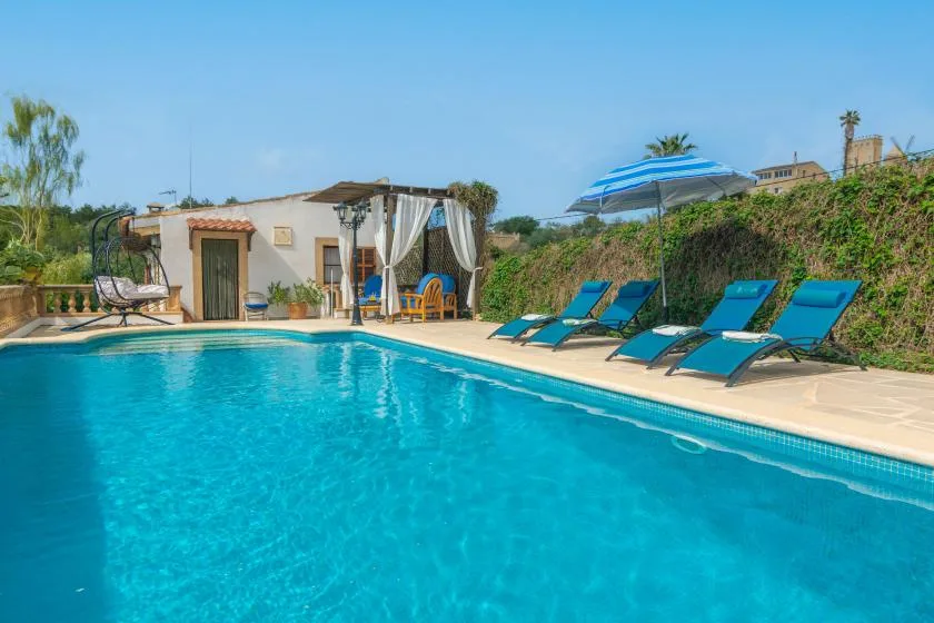 An outdoor swimming pool with blue lounge seating beside a small white building.