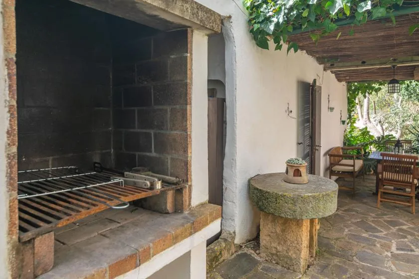 A covered patio has a built-in grill, a stone table, and outdoor seating.
