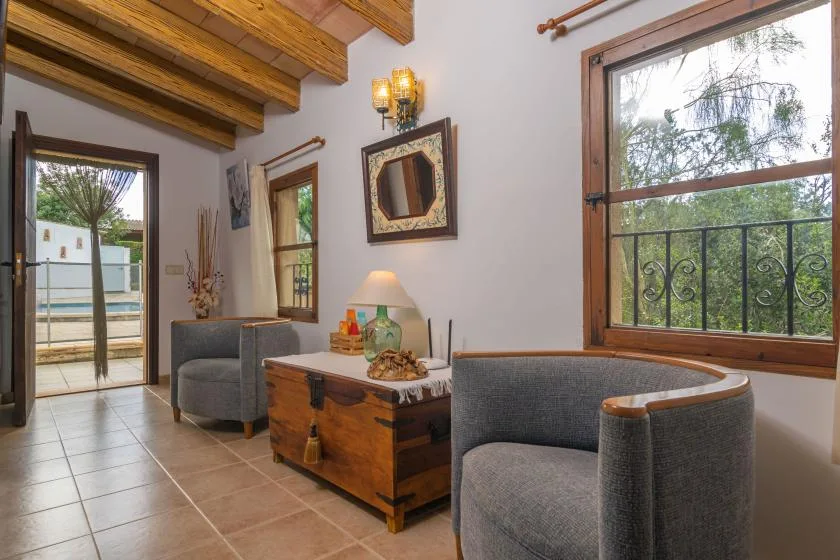 A sitting room with cushioned seating, a wooden chest, and large windows.