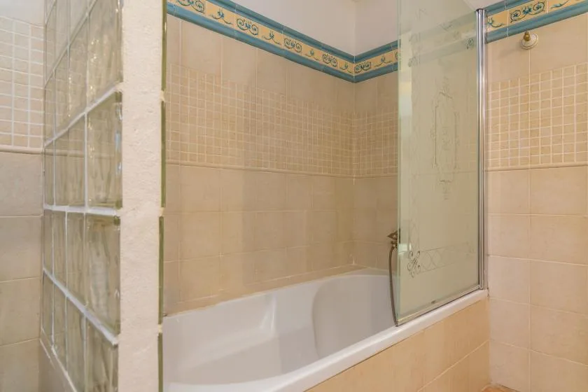 A tiled bathroom with a bathtub and glass shower screen.