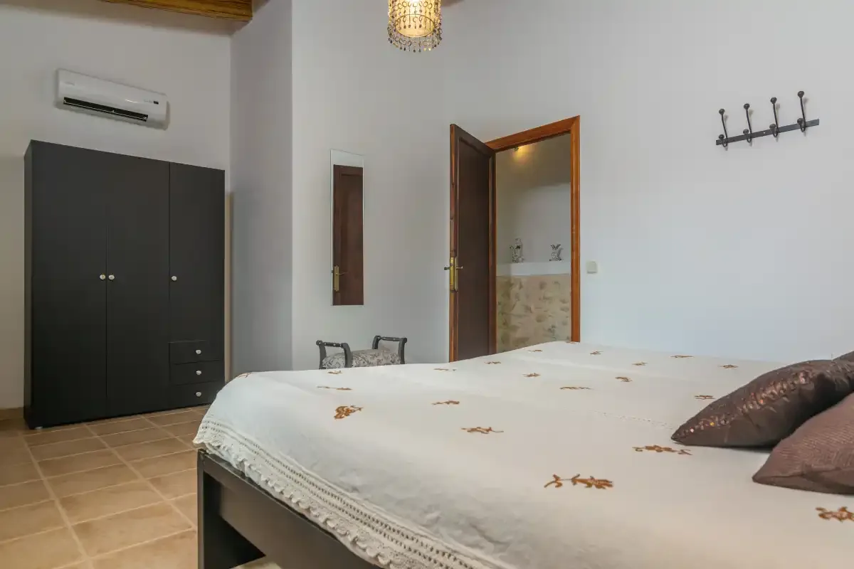 A bedroom with a bed, a dark wardrobe, and an open doorway.