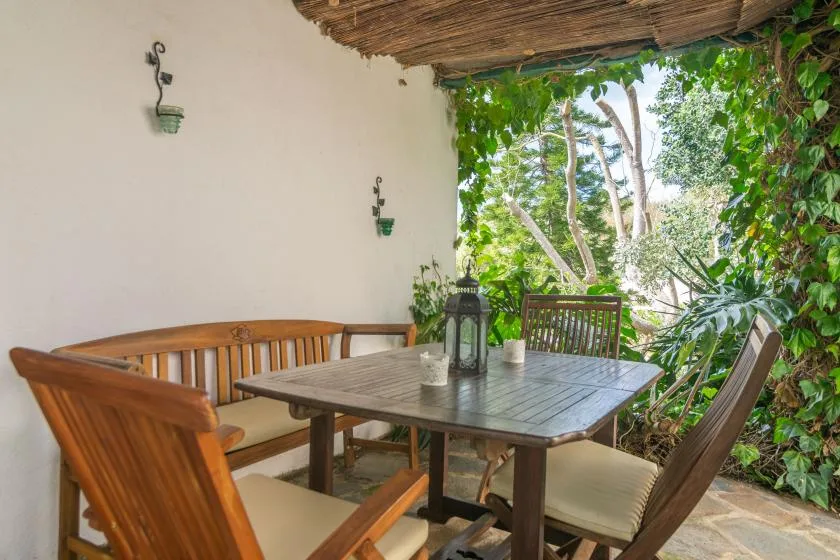 An outdoor dining area with a wooden table and seating beneath a leafy pergola.