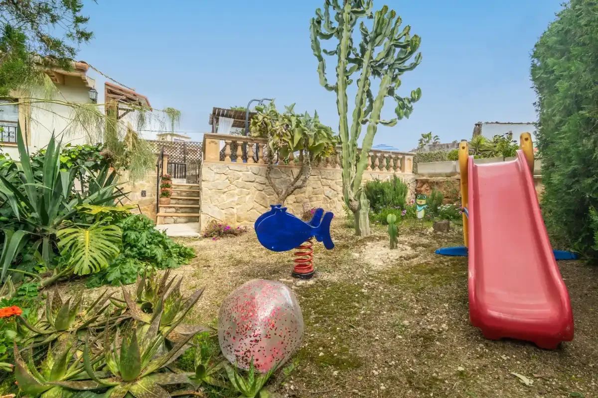 A garden play area with a red slide and colorful spring rider.