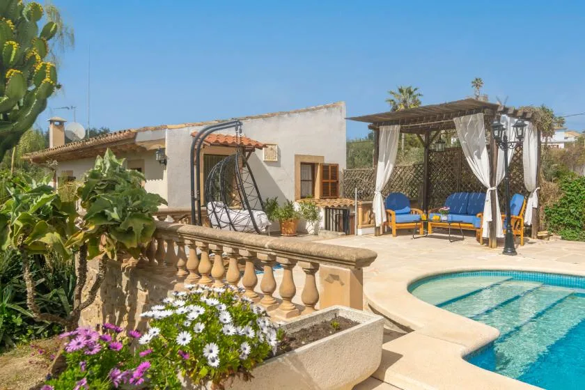 A sunny outdoor pool area with a shaded seating pergola beside the house.