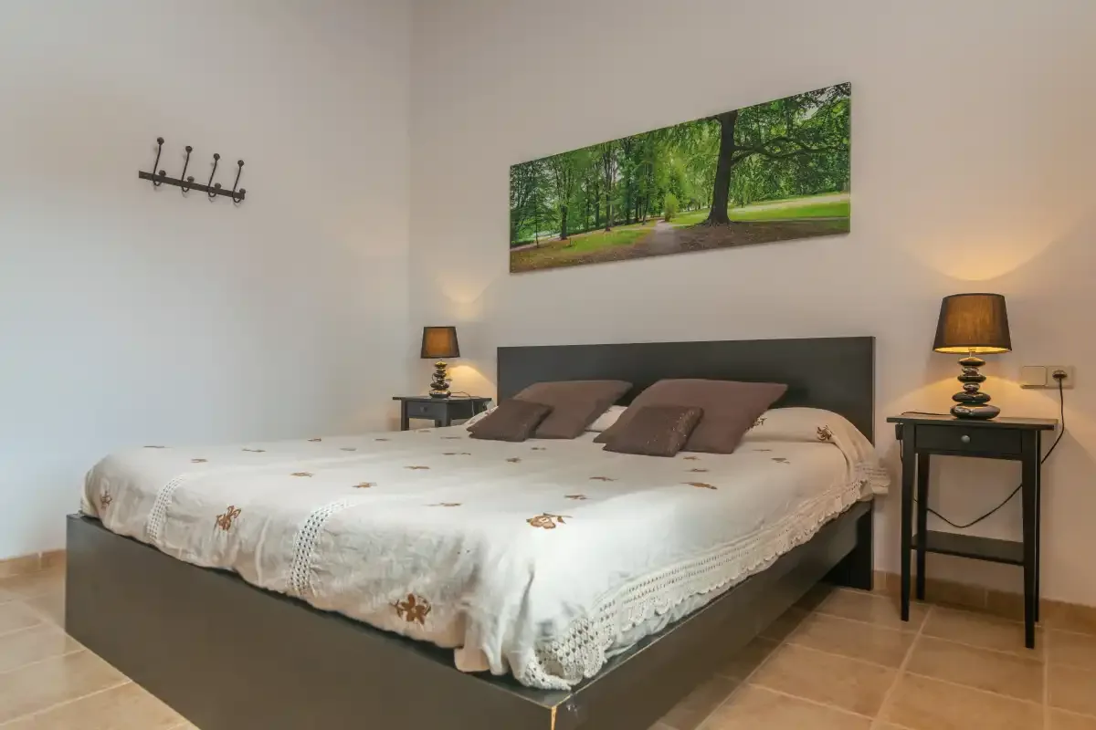 A bedroom with a large bed, bedside tables, and a landscape print above the headboard.