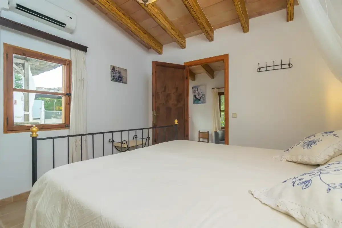 A bedroom with a bed, a window, and exposed wooden ceiling beams.