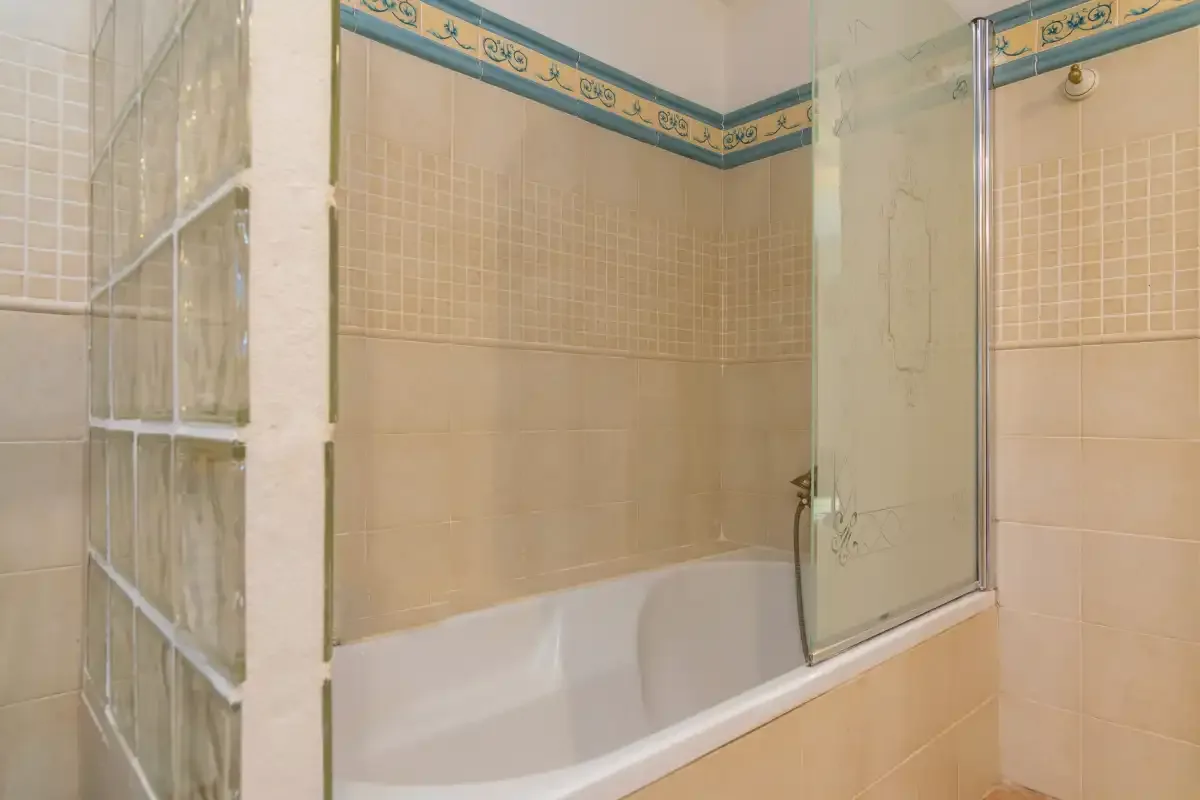 A tiled bathroom with a bathtub and glass shower screen.
