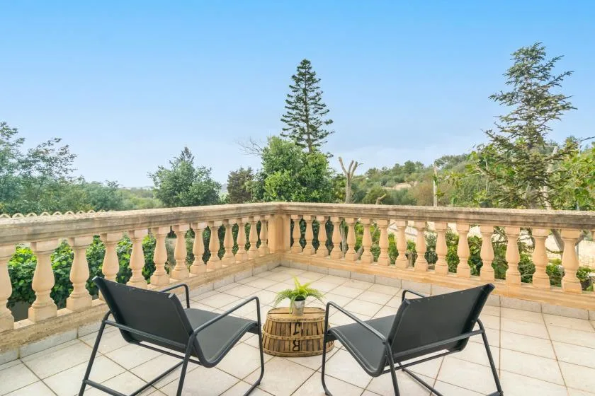 A tiled outdoor terrace with two lounge seats and views of trees.