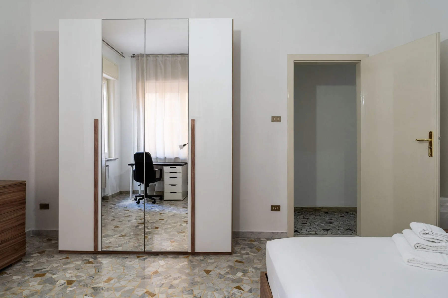 A bedroom with a mirrored wardrobe, desk, and open doorway.