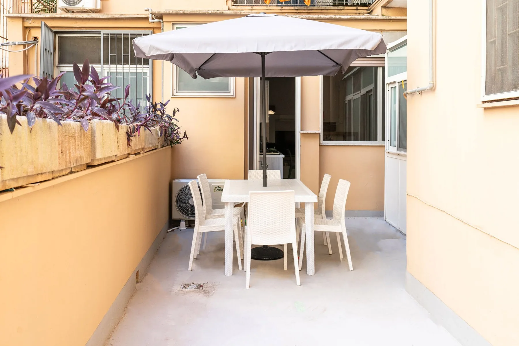 An outdoor patio has a white dining table and seating beneath a large umbrella.