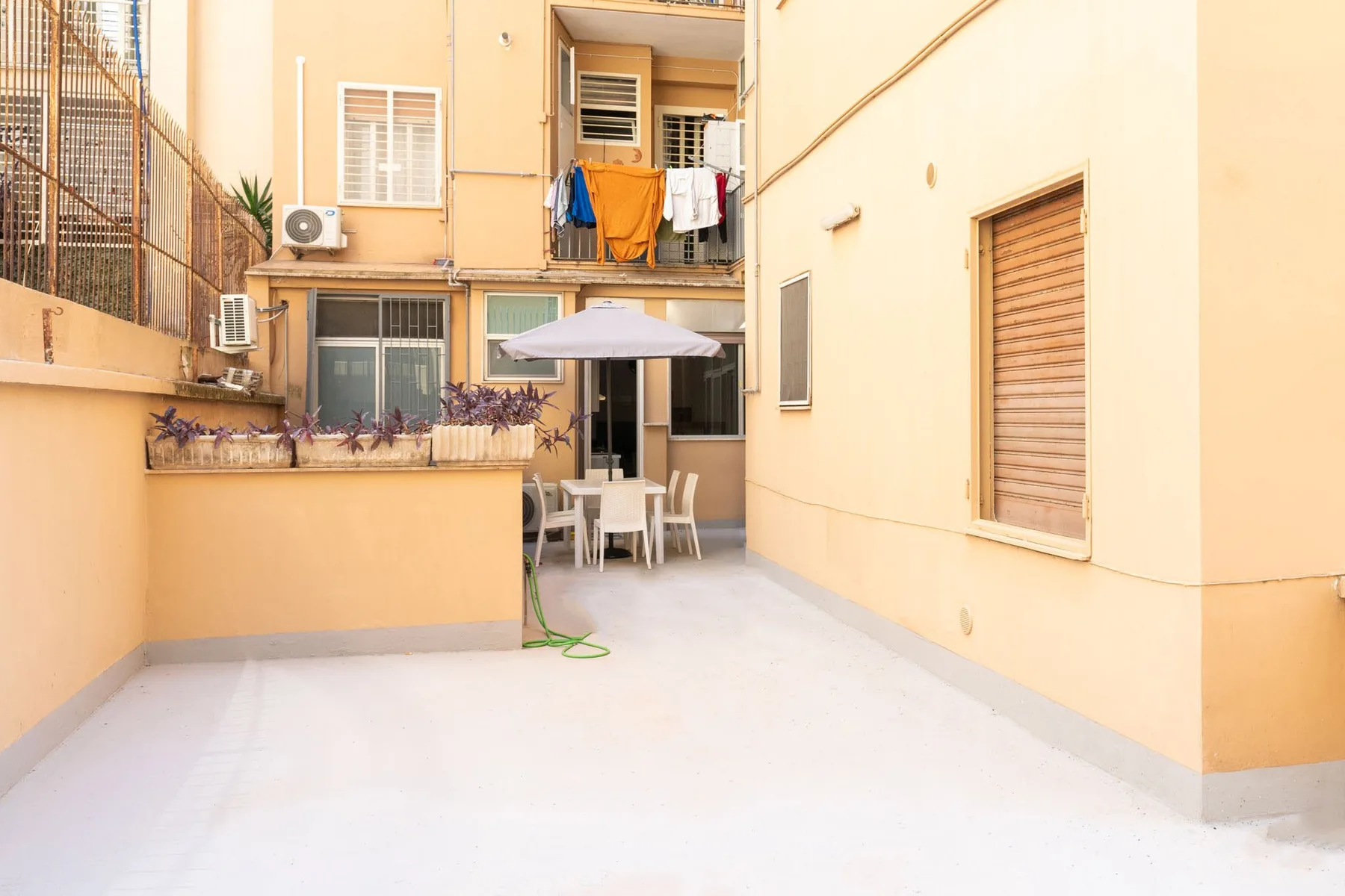 A paved courtyard with outdoor seating and an umbrella beside apartment buildings.