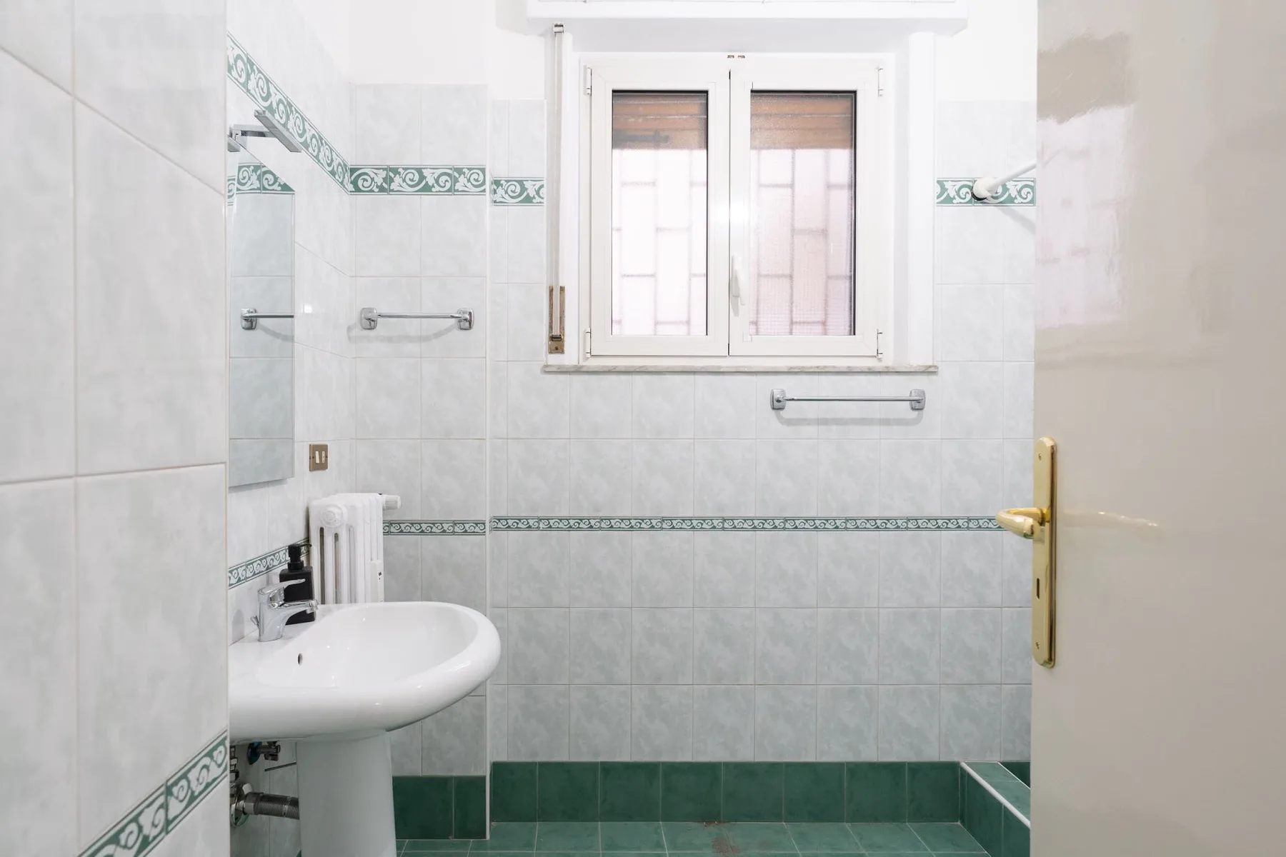 A tiled bathroom with a pedestal sink and a window.
