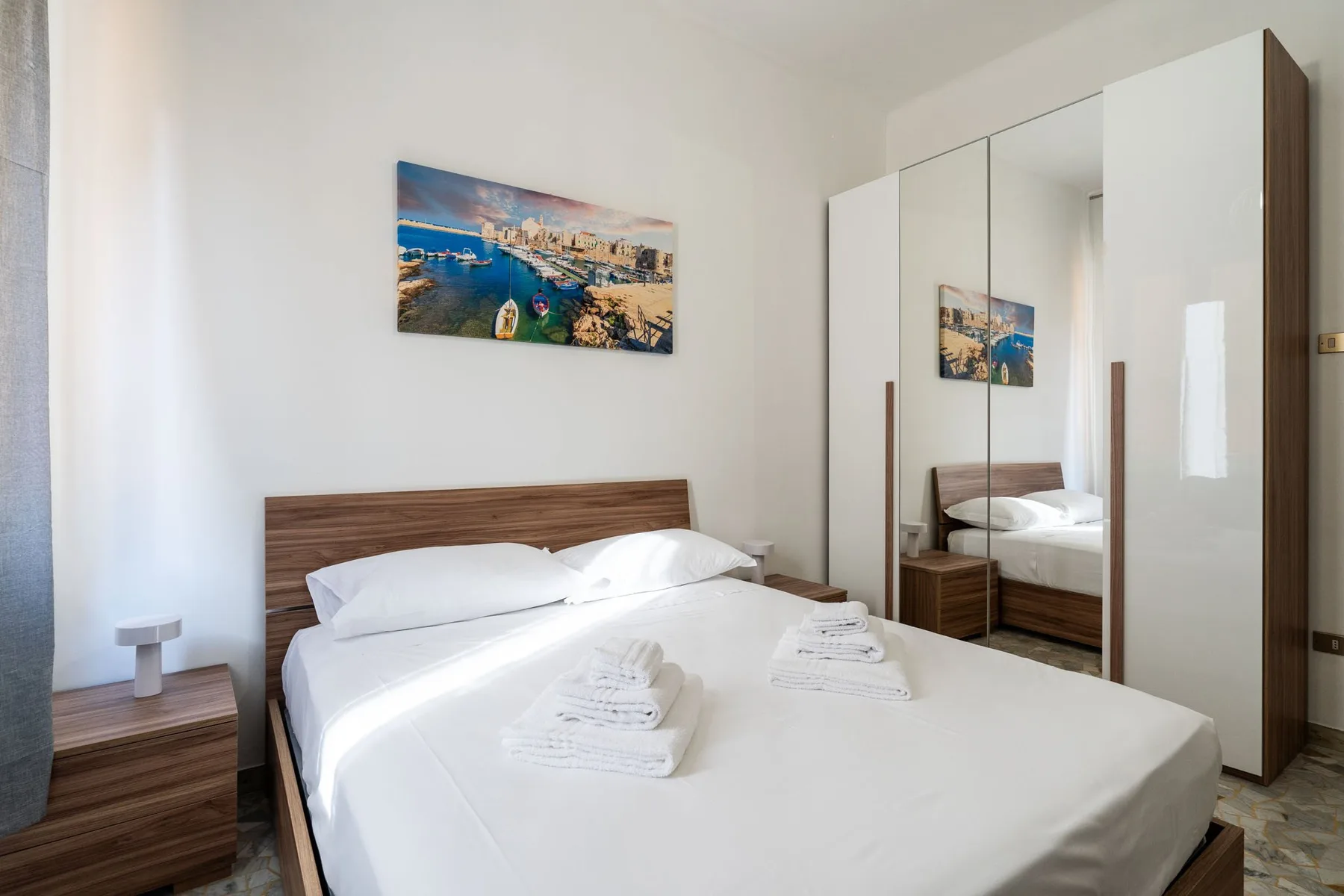 A bedroom with a neatly made bed, folded towels, and a mirrored wardrobe.