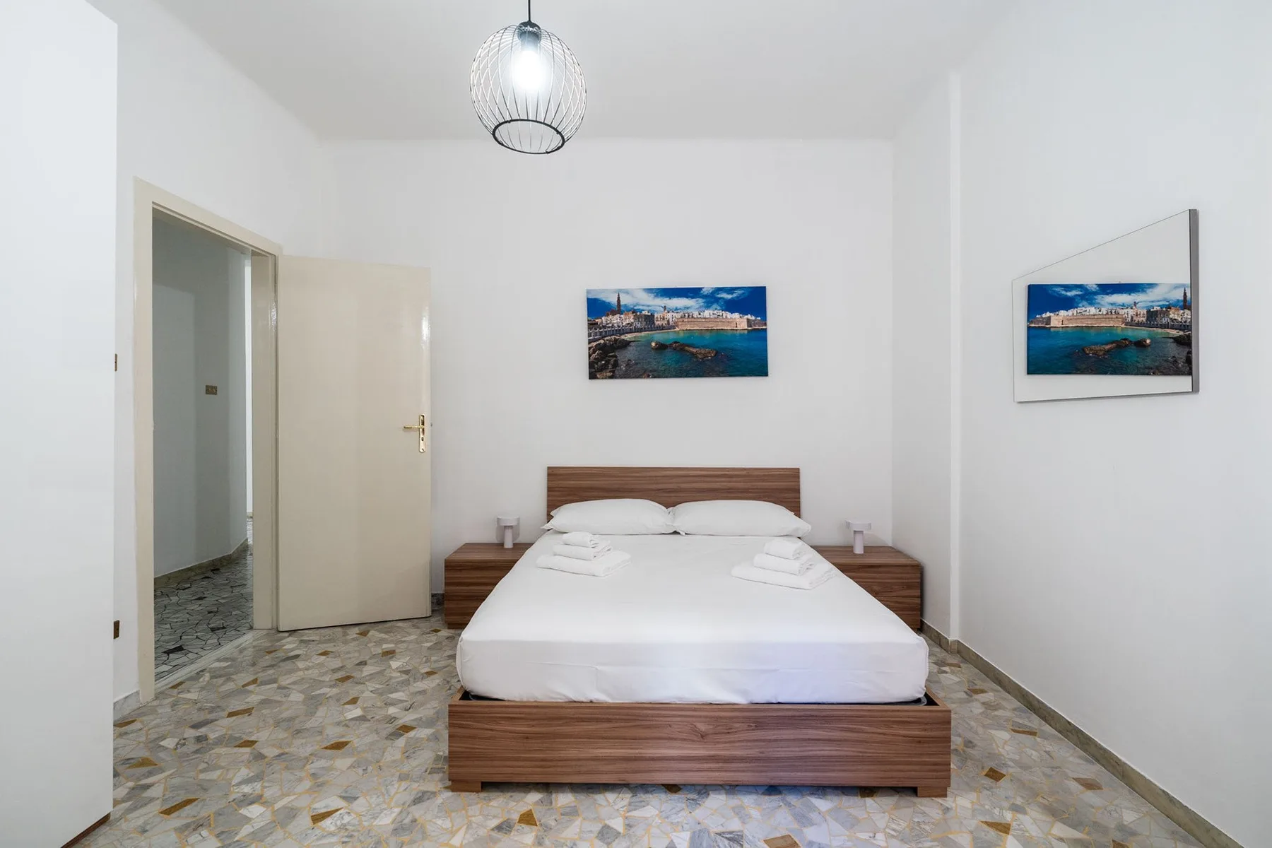 A bedroom with a neatly made bed and framed coastal photographs on the walls.