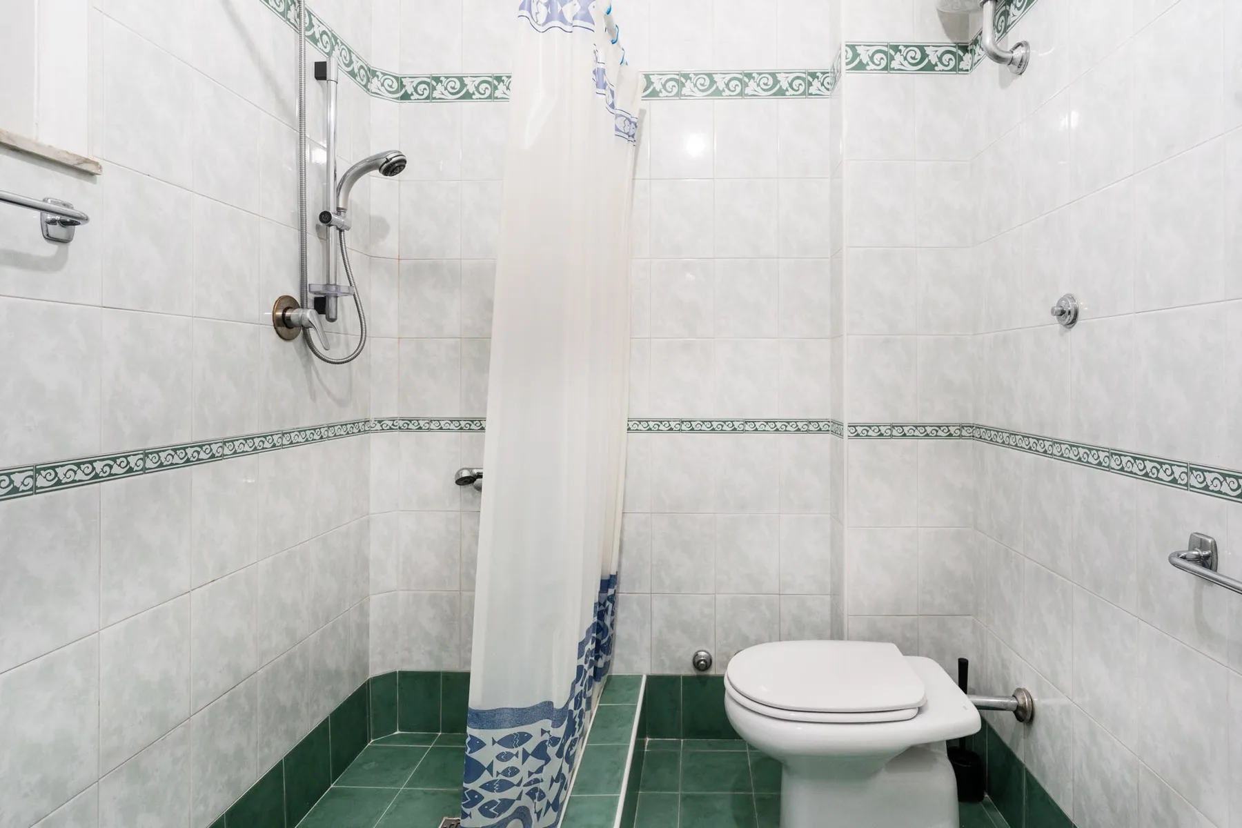 A tiled bathroom with a shower curtain and toilet.