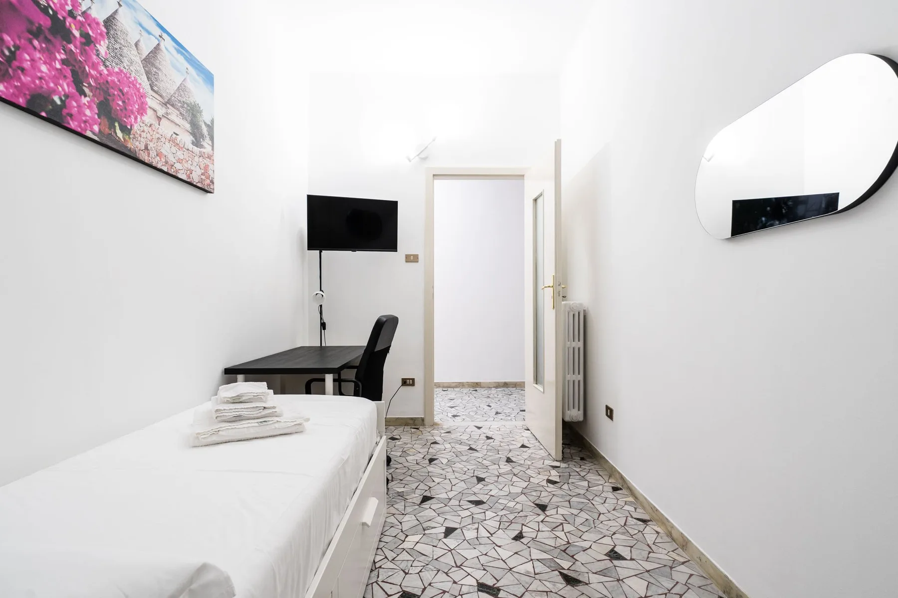 A bright bedroom with a single bed, desk, and wall-mounted television.